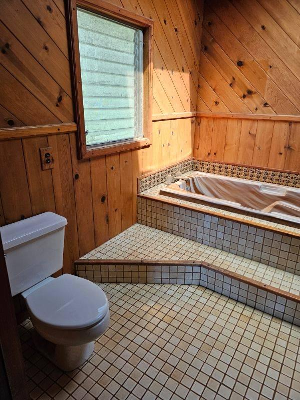 bathroom with tile patterned floors, a bathing tub, toilet, and wooden walls