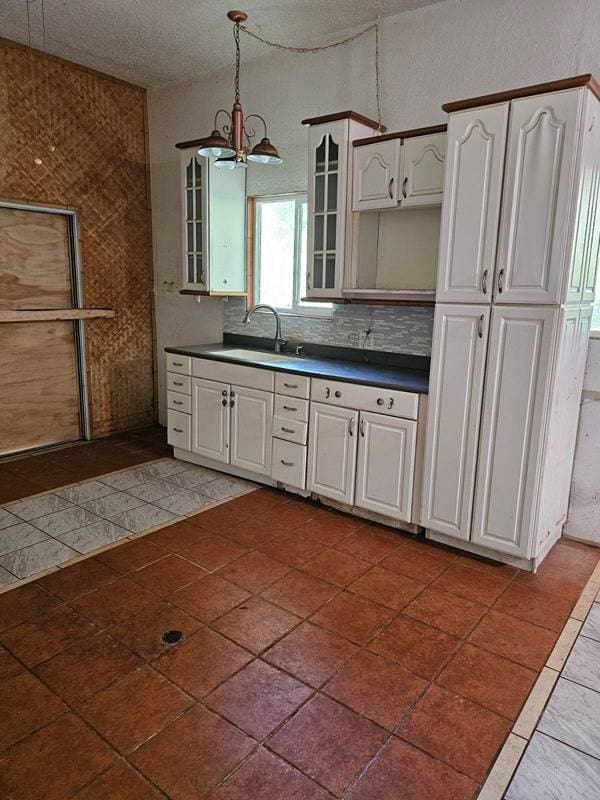 kitchen featuring backsplash, sink, decorative light fixtures, a notable chandelier, and white cabinetry