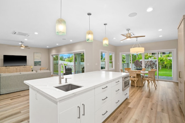 kitchen featuring white cabinets, decorative light fixtures, sink, and a kitchen island with sink