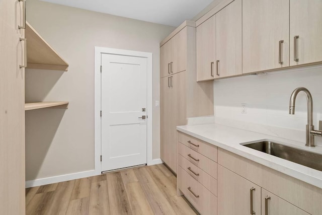 kitchen featuring light brown cabinetry, light wood-type flooring, backsplash, and sink