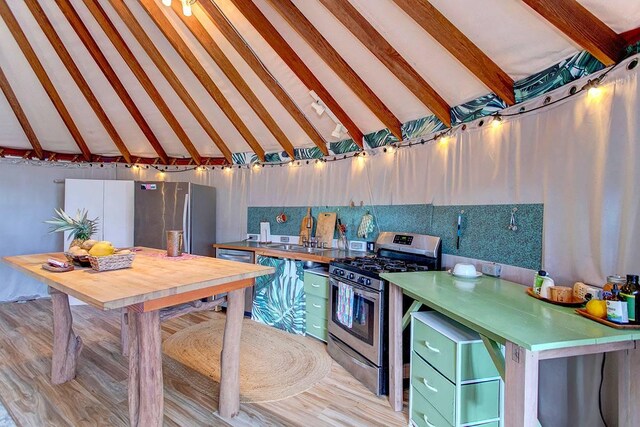 kitchen featuring green cabinets, sink, lofted ceiling with beams, and appliances with stainless steel finishes