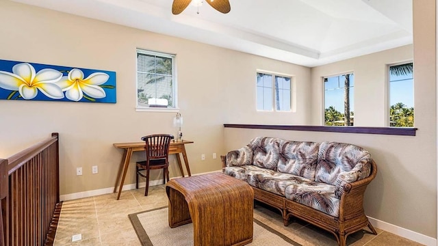 living area with a raised ceiling, ceiling fan, and light tile patterned floors