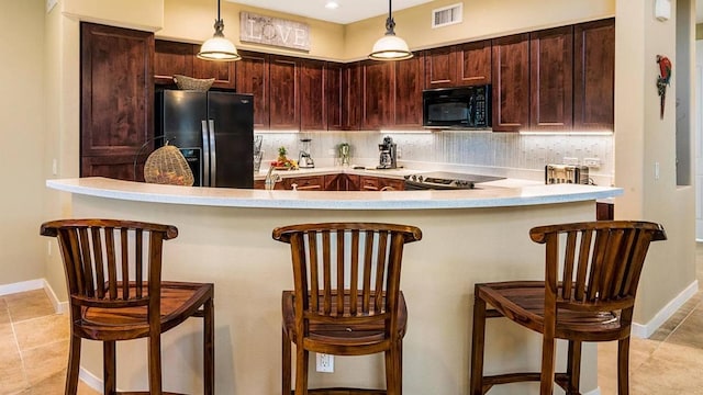 kitchen with black appliances, hanging light fixtures, decorative backsplash, a kitchen bar, and kitchen peninsula