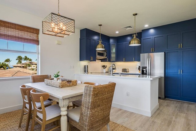 kitchen featuring hanging light fixtures, a breakfast bar, blue cabinets, light wood-type flooring, and stainless steel appliances