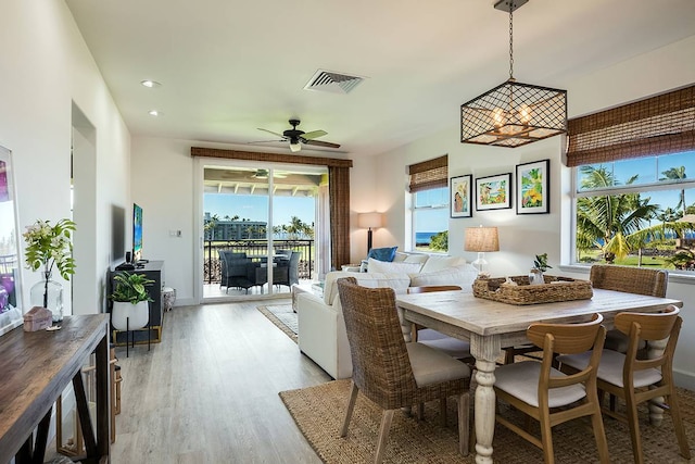 dining space with ceiling fan with notable chandelier and light wood-type flooring