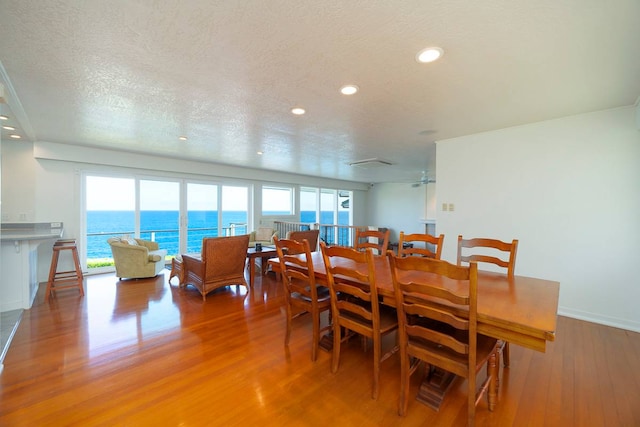 dining area with a water view, a textured ceiling, and wood-type flooring