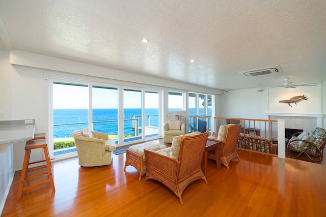 living room with a tiled fireplace, hardwood / wood-style floors, ceiling fan, a water view, and a textured ceiling