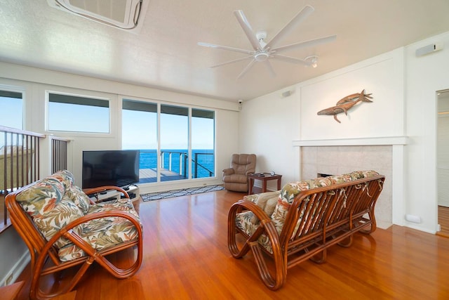 living room featuring ceiling fan, a fireplace, wood-type flooring, a water view, and a wealth of natural light