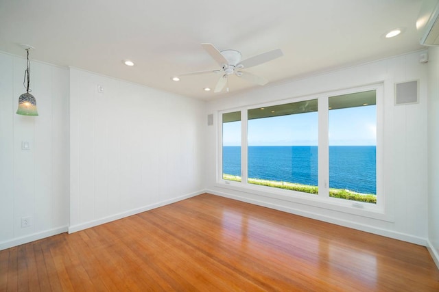 spare room featuring a wall unit AC, a water view, wood-type flooring, and ceiling fan