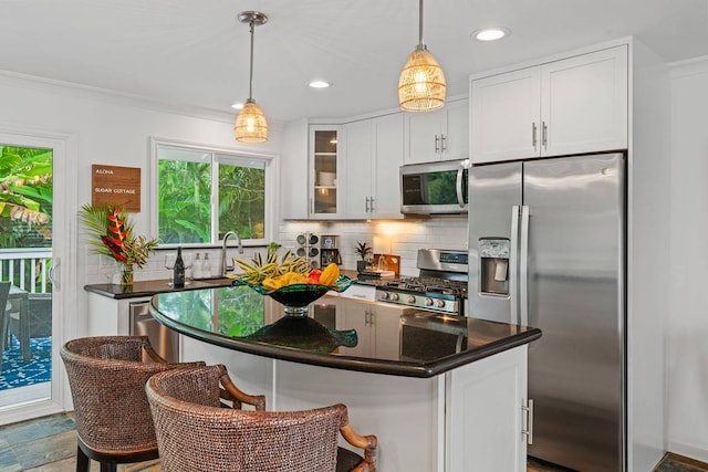 kitchen with pendant lighting, white cabinets, appliances with stainless steel finishes, a breakfast bar, and backsplash