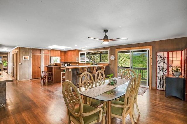 dining area with ceiling fan, wooden walls, dark hardwood / wood-style floors, and a skylight