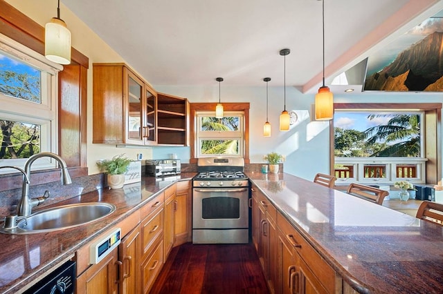 kitchen with sink, dark stone counters, dark wood-type flooring, stainless steel range with gas stovetop, and decorative light fixtures