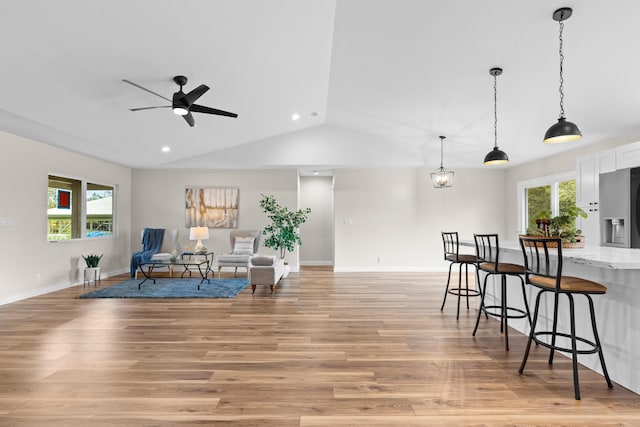 living area with ceiling fan, vaulted ceiling, a healthy amount of sunlight, and light wood-type flooring