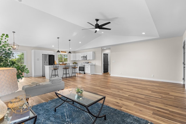 living room featuring vaulted ceiling, ceiling fan with notable chandelier, and light hardwood / wood-style floors