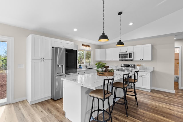 kitchen featuring stainless steel appliances, a center island, light stone countertops, white cabinets, and decorative light fixtures