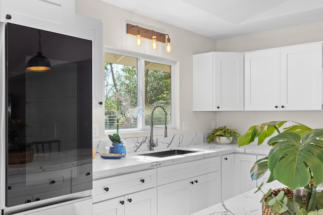 kitchen featuring white cabinetry, decorative light fixtures, light stone countertops, and sink