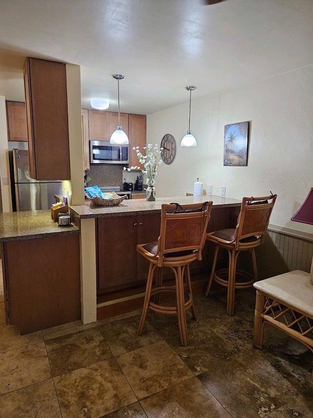 kitchen featuring kitchen peninsula, backsplash, appliances with stainless steel finishes, dark tile patterned flooring, and pendant lighting