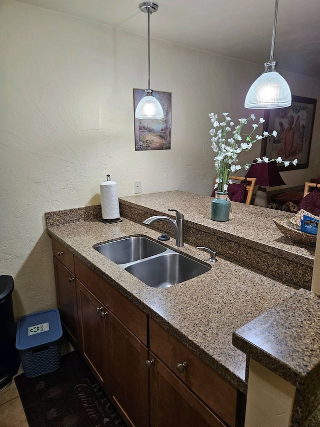 kitchen with sink, light stone counters, hanging light fixtures, and dark brown cabinets