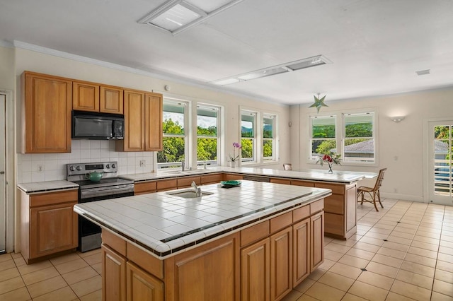 kitchen featuring a kitchen island with sink, a healthy amount of sunlight, tile countertops, and stainless steel electric range oven