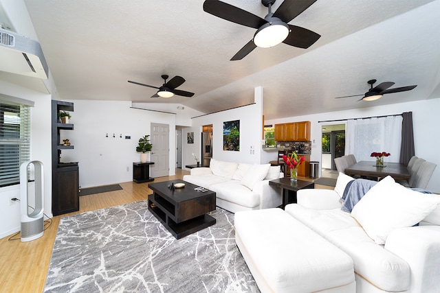 living room featuring lofted ceiling, light hardwood / wood-style floors, ceiling fan, and a textured ceiling