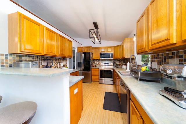 kitchen with appliances with stainless steel finishes, a breakfast bar, tasteful backsplash, light wood-type flooring, and sink