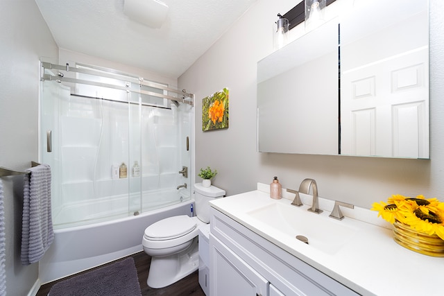 full bathroom with wood-type flooring, a textured ceiling, combined bath / shower with glass door, vanity, and toilet