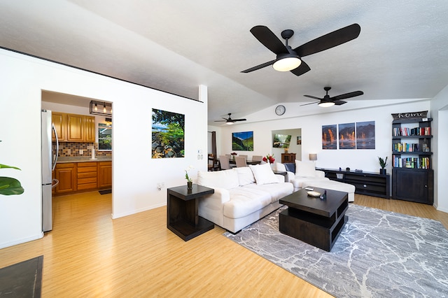 living room with a textured ceiling, light hardwood / wood-style floors, vaulted ceiling, and ceiling fan