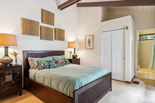 bedroom featuring connected bathroom, a closet, light hardwood / wood-style flooring, and vaulted ceiling with beams