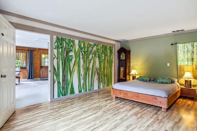 bedroom featuring light hardwood / wood-style floors, crown molding, and wooden walls