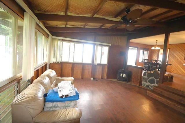 interior space featuring lofted ceiling with beams, ceiling fan with notable chandelier, a wood stove, and a wealth of natural light