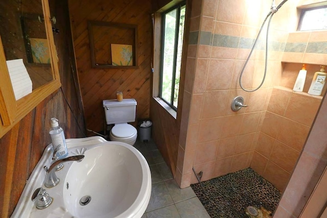 bathroom featuring wooden walls, tile flooring, sink, and tiled shower