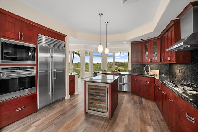 kitchen with backsplash, beverage cooler, wall chimney range hood, a kitchen island, and built in appliances