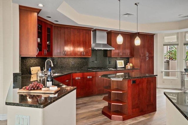 kitchen with dark stone counters, decorative light fixtures, sink, light hardwood / wood-style flooring, and wall chimney exhaust hood