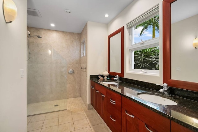 bathroom featuring oversized vanity, a tile shower, tile floors, and dual sinks