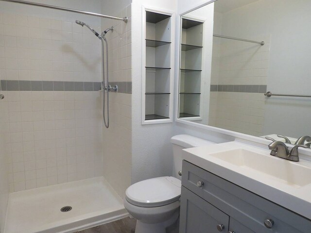 bathroom featuring toilet, tiled shower, vanity with extensive cabinet space, and hardwood / wood-style flooring