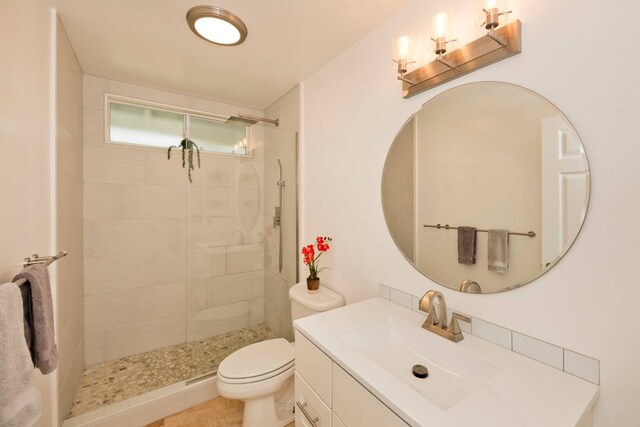 bathroom with toilet, a tile shower, and vanity