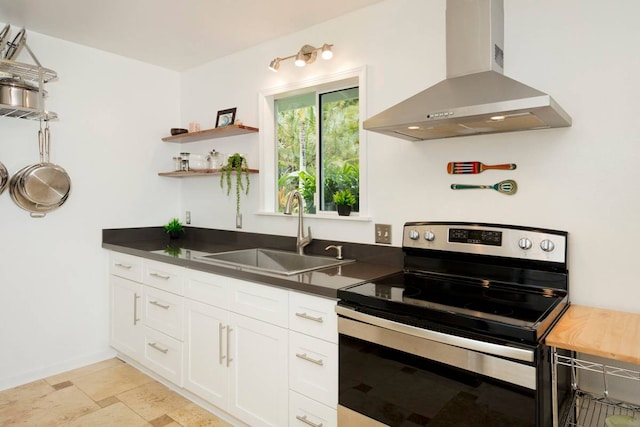 kitchen with light tile floors, stainless steel electric range, wall chimney exhaust hood, white cabinets, and sink