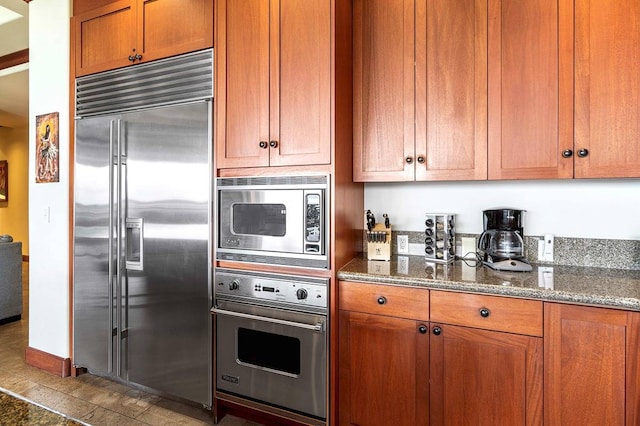 kitchen featuring built in appliances, tile floors, and dark stone counters