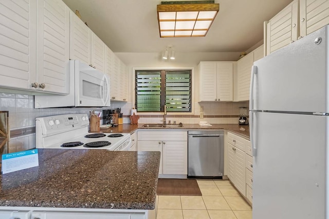 kitchen featuring dark stone counters, light tile floors, backsplash, white appliances, and sink