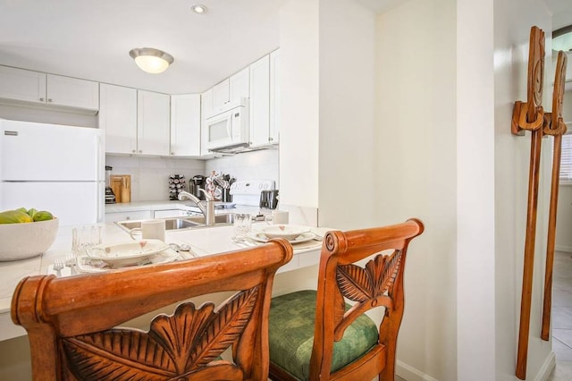 kitchen featuring light tile floors, tasteful backsplash, white appliances, white cabinetry, and sink