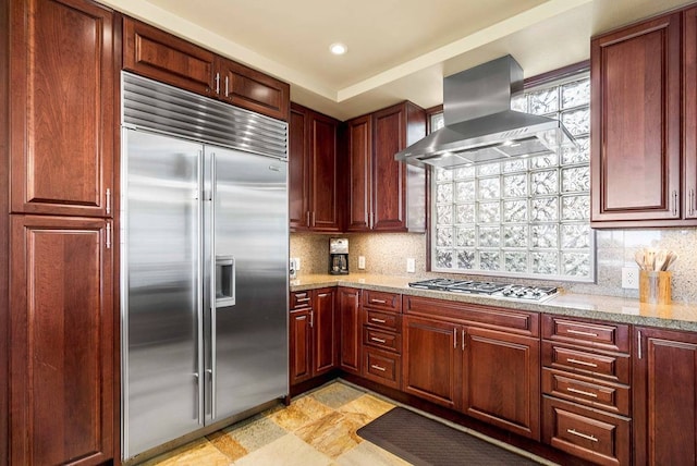 kitchen with light stone countertops, appliances with stainless steel finishes, backsplash, and wall chimney exhaust hood