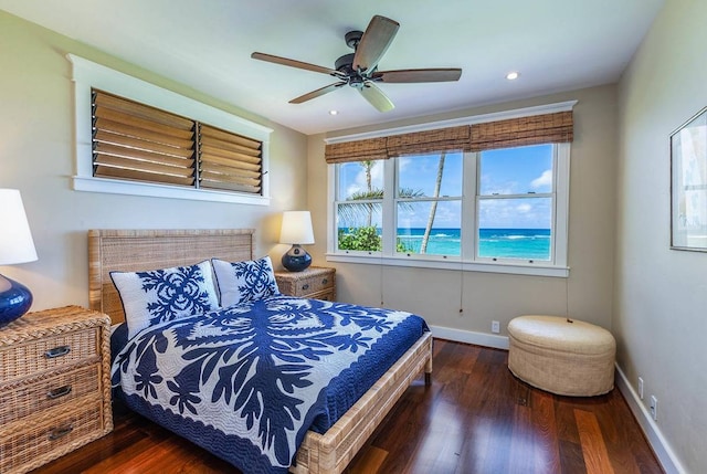 bedroom with dark hardwood / wood-style floors, ceiling fan, and a water view