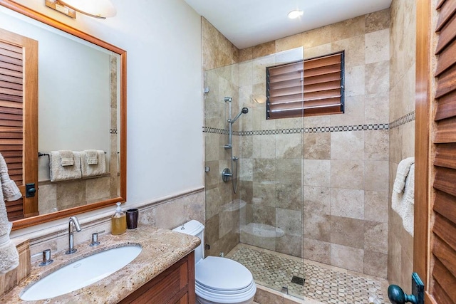 bathroom with toilet, a shower with door, vanity, and tile walls