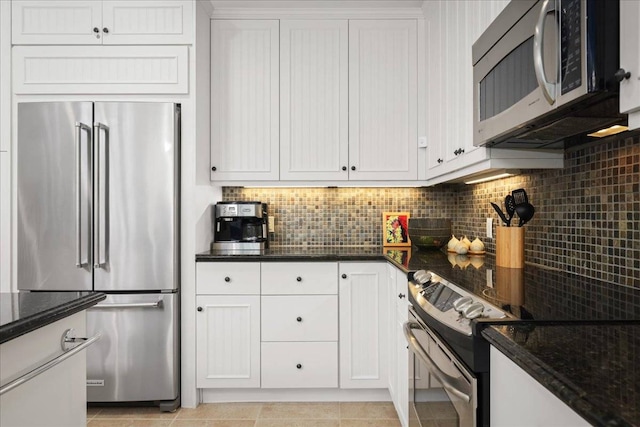 kitchen featuring stainless steel appliances, light tile floors, dark stone counters, white cabinetry, and backsplash