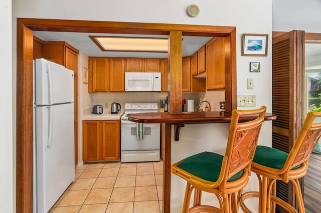 kitchen with a kitchen bar, light tile floors, and white appliances