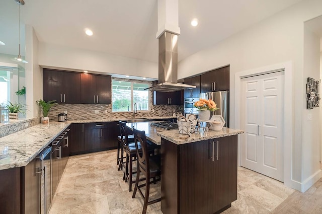 kitchen with appliances with stainless steel finishes, light stone counters, a kitchen island, backsplash, and island range hood