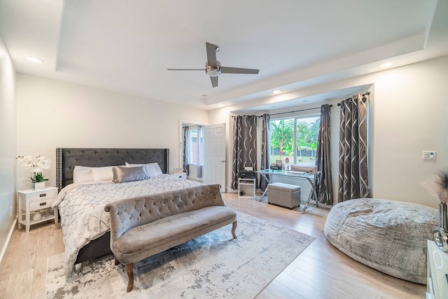 bedroom featuring light hardwood / wood-style flooring, ceiling fan, and a tray ceiling