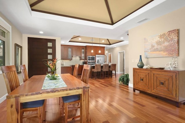 dining room featuring a raised ceiling and light hardwood / wood-style flooring