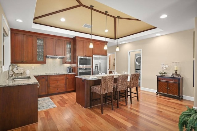 kitchen with a raised ceiling, sink, stacked washer and dryer, hanging light fixtures, and stainless steel appliances