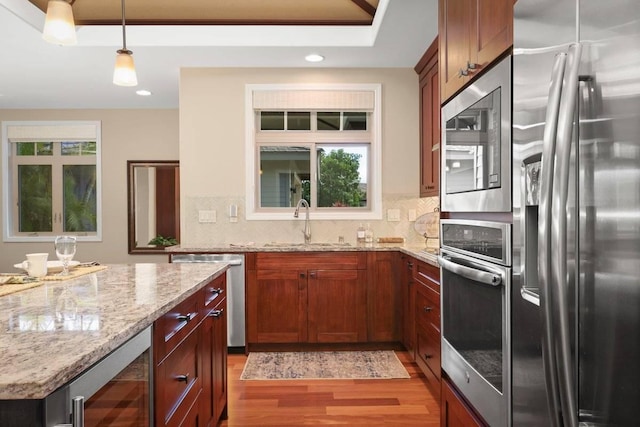 kitchen with pendant lighting, appliances with stainless steel finishes, light stone countertops, beverage cooler, and light wood-type flooring